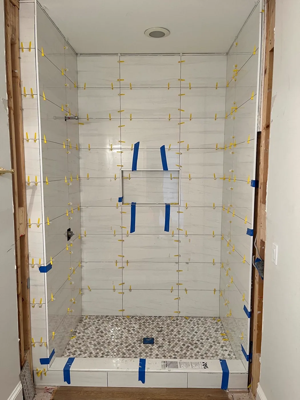 Colocación de azulejo en proceso en la ducha durante una remodelación de baño principal, con separadores visibles entre las piezas, Metro Atlanta